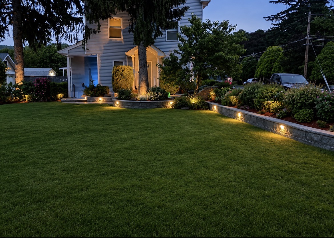 Sierra landscape lighting illuminating a finished lawn, planting beds and retaining wall at dusk
